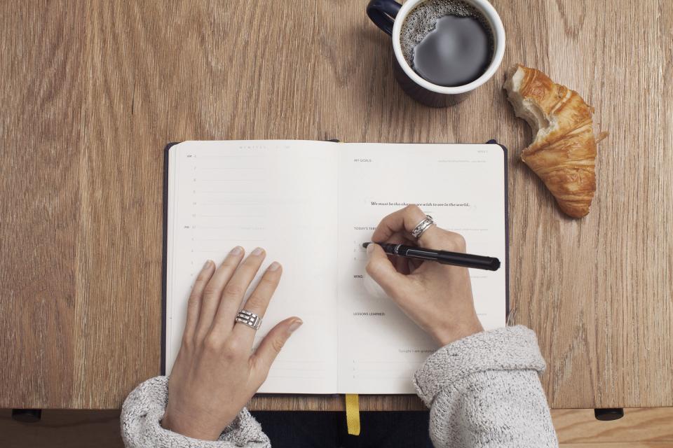Hands writing in a journal beside coffee